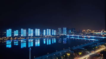 A nighttime cityscape with illuminated buildings reflecting on a river.
