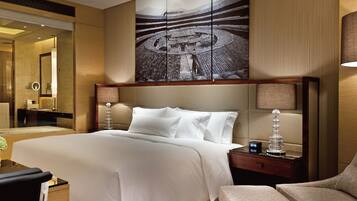 Habitación de hotel con una cama grande, una mesita de noche con lámpara, una silla y una obra de arte de gran tamaño en la pared.