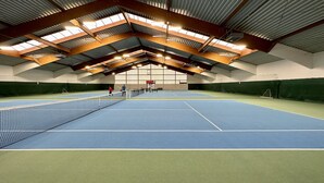 Een binnentennisbaan met een hoge plafond, zichtbare balken en kunstlicht.