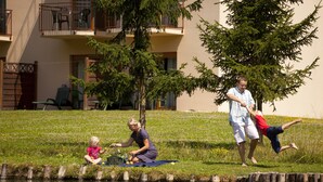 Een gazon met een waterpartij, bomen en een gebouw met balkons op de achtergrond.