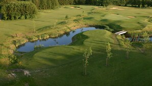 Een golfbaan met een vijver, bomen en een klein gebouw.