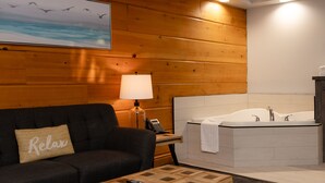 A room with a black sofa, a wooden coffee table, a lamp, a telephone, and a large bathtub. - Terrace Suites (Callander)