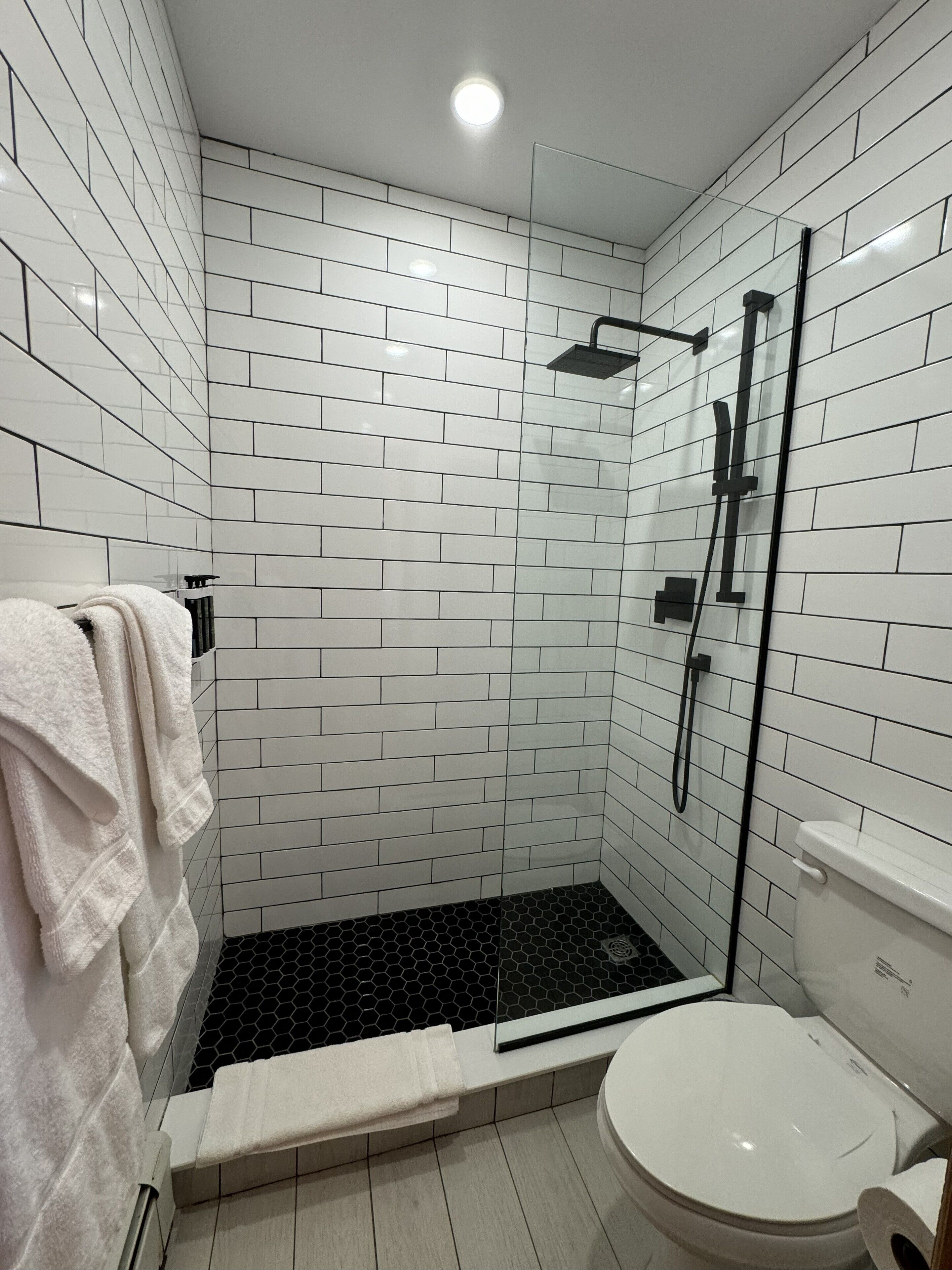 A modern bathroom with white subway tiles, a glass shower enclosure, a white toilet, and a towel rack with towels.
