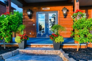 A wooden building with a sign reading "OFFICE" above the entrance. There are two potted plants with red flowers in front of the entrance. - Terrace Suites (Callander)