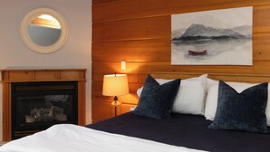 A bedroom with a wooden headboard, a fireplace, a round mirror, and a painting of a mountain landscape. - Terrace Suites (Callander)