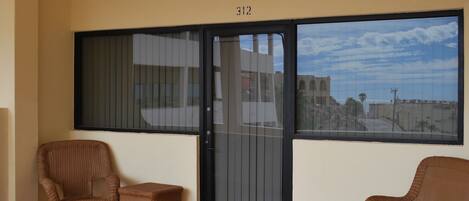 A balcony with wicker chairs, a small table, and a sliding glass door with a city view.