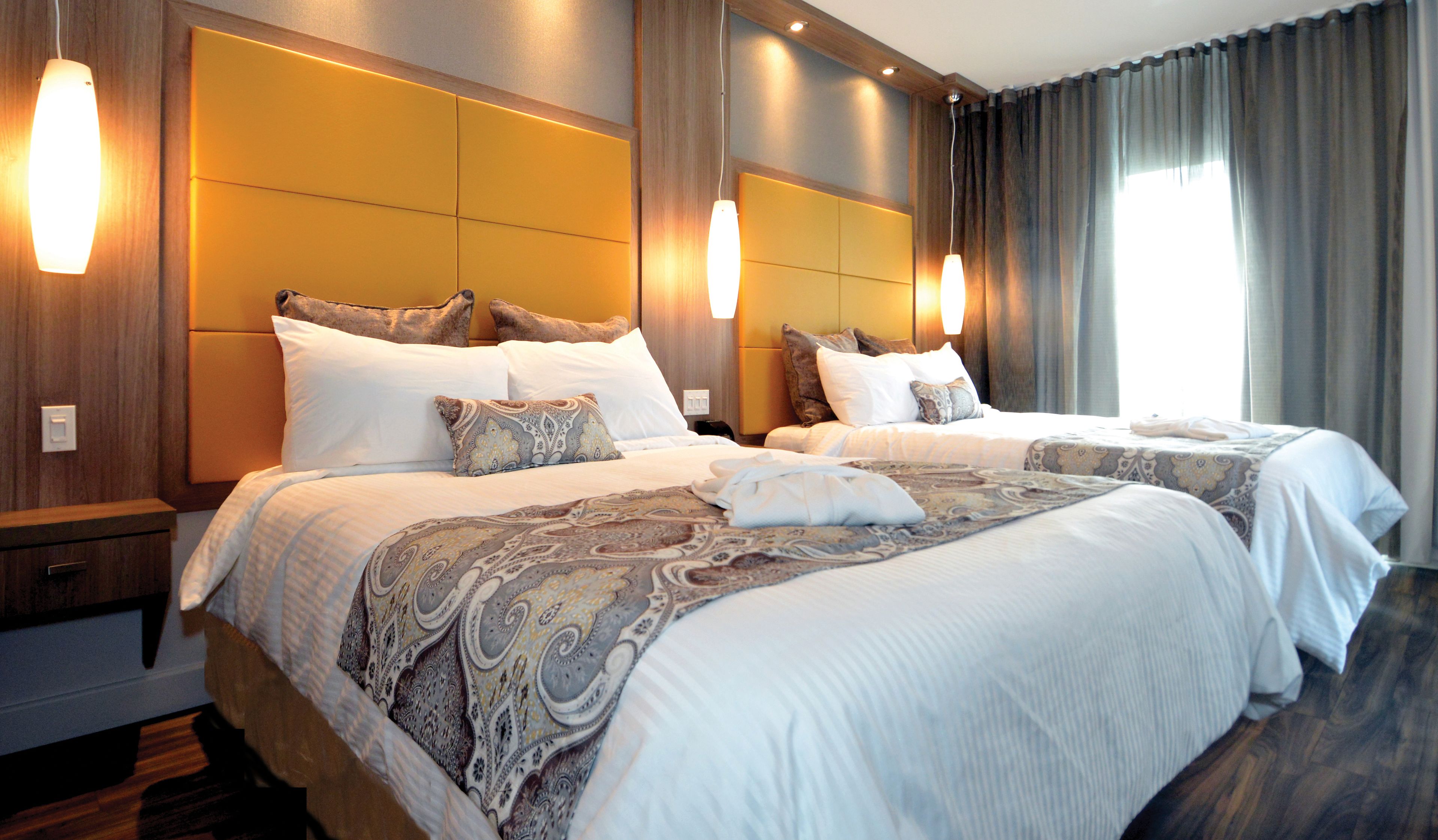 Habitación de hotel con dos camas, cada una con cabecero, mesitas de noche y lámparas.
