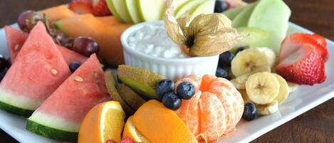 Una bandeja de frutas con diversas frutas y un tazón pequeño de yogur.