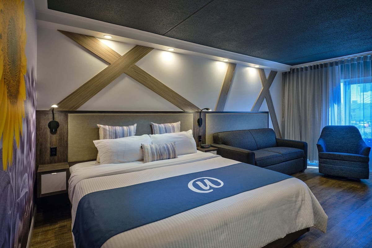 Ein modernes Hotelzimmer mit einem großen Bett, einer Couch, einem Sessel und Blick auf die Stadt.