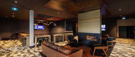 A modern lobby with a patterned carpet, leather seating, a fireplace, and a TV screen.
