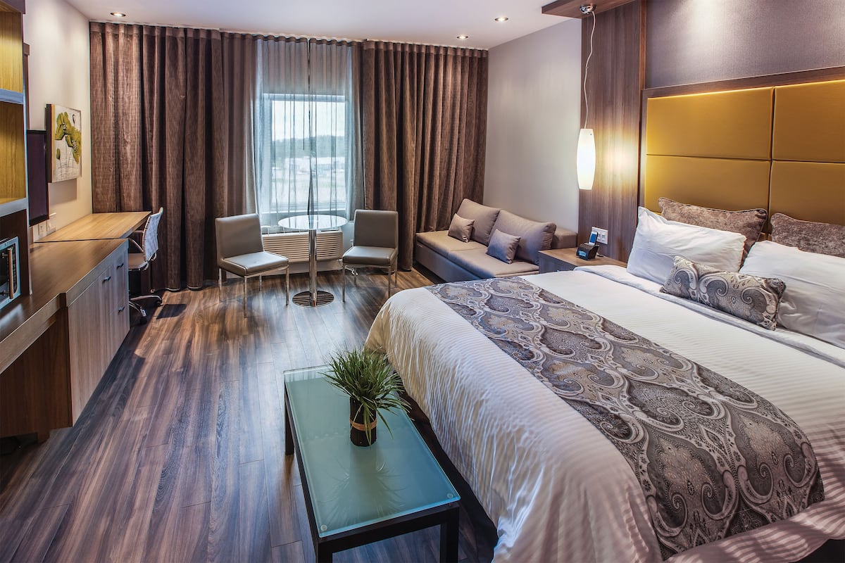 Ein Hotelzimmer mit Bett, Sofa, Schreibtisch, Stuhl und einem kleinen Tisch mit Pflanze.