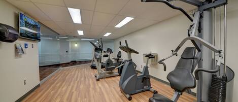 A gym with exercise equipment, wooden flooring, and a large mirror.