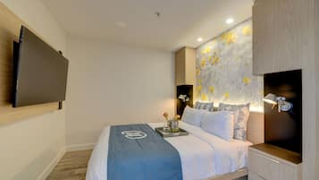 Una habitación de hotel moderna con cama, televisor de pantalla plana, mesita de noche con lámpara y un adorno en la pared.