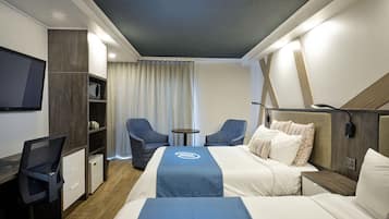 A hotel room with a bed, two chairs, a desk, a TV, and a small table.