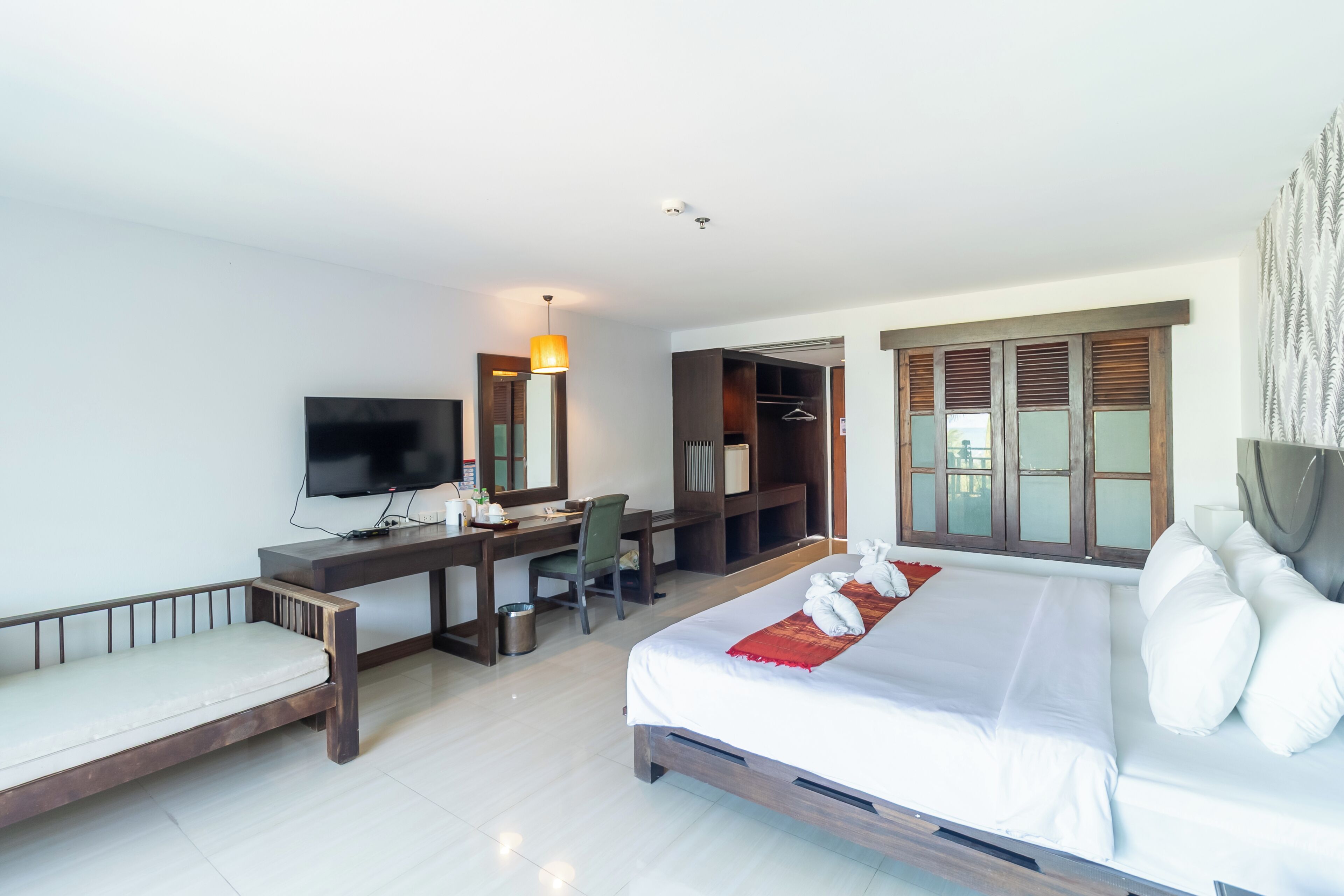 Quarto de hotel com uma cama, uma escrivaninha com cadeira, televisão e guarda-roupa.