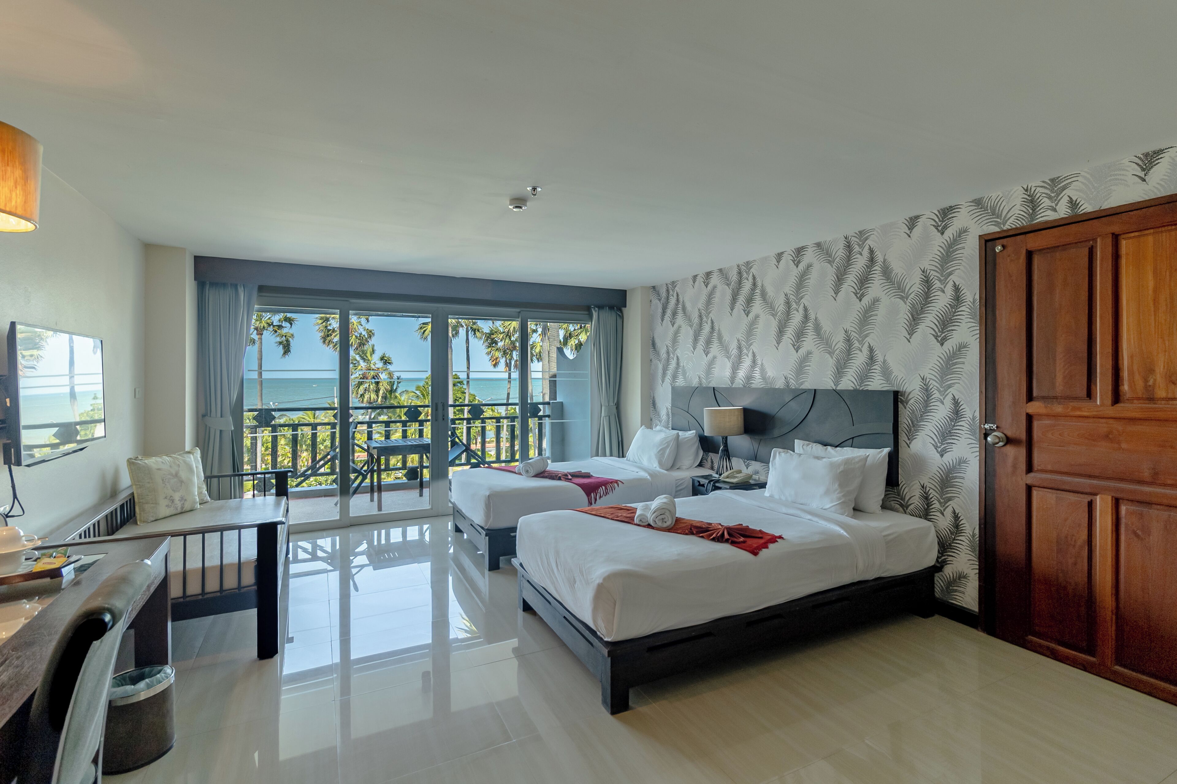 Een hotelkamer met een bed, bureau, stoel, televisie en een balkon met uitzicht op zee.