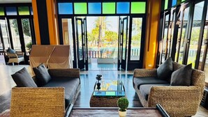 A spacious lobby with wicker furniture, a glass coffee table, and large windows offering a view of the outdoors. - Pattawia Resort & Spa (Pranburi)