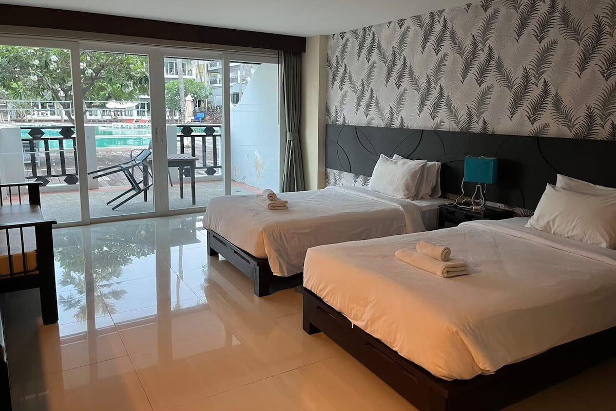 Ein Hotelzimmer mit zwei Betten, einem großen Fenster, einem Balkon mit Tisch und Stühlen sowie einer Wand mit Musterung.
