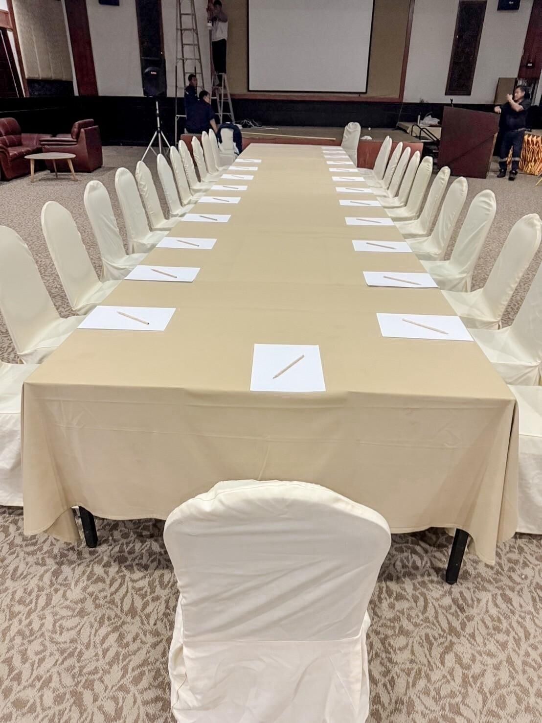 A conference room with a long table, white chairs, and a projector screen.