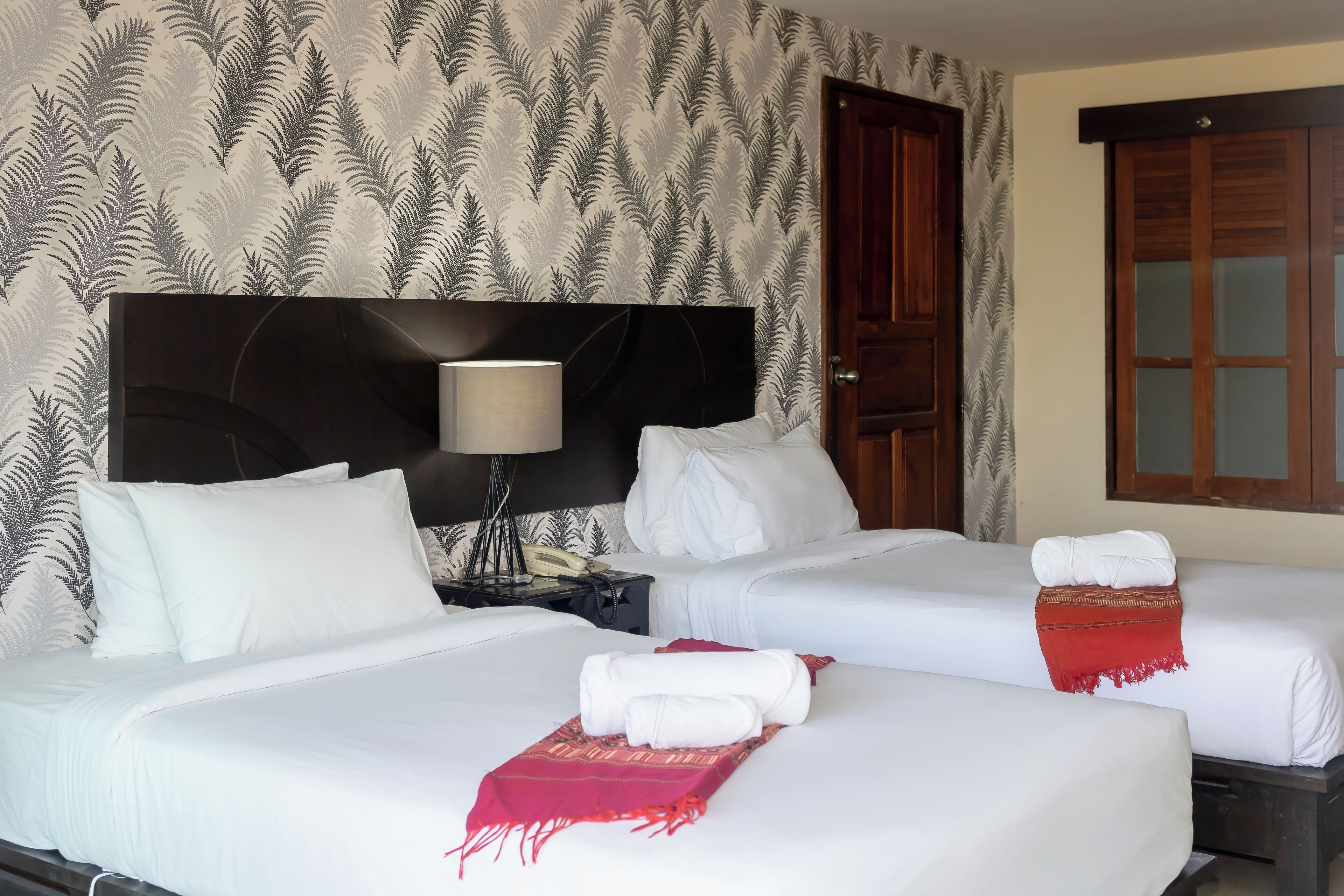 Habitación de hotel con dos camas, una mesita de noche, una lámpara y una puerta.