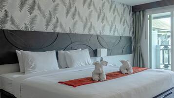A hotel room with a large bed, white bedding, a red throw blanket, and a headboard with a leaf pattern.