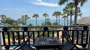 A balcony with a table and chairs, overlooking a beach and palm trees. - Pattawia Resort & Spa (Pranburi)