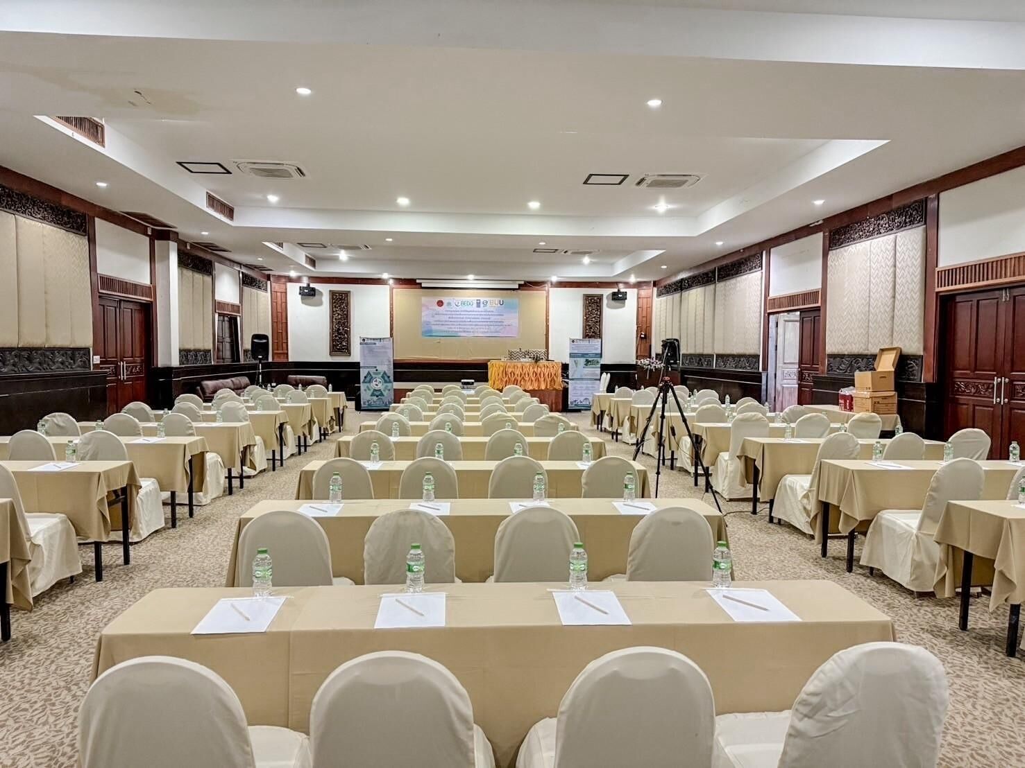 A conference room with rows of tables and chairs, a podium, and a projection screen.