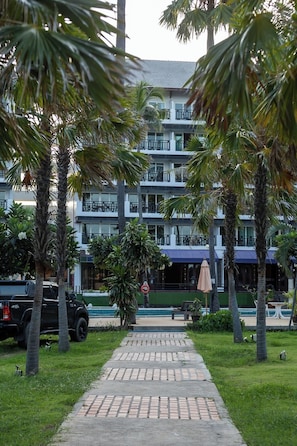 A pathway leading to a multi-story building with balconies, surrounded by palm trees and a parked vehicle. - Pattawia Resort & Spa (Pranburi)