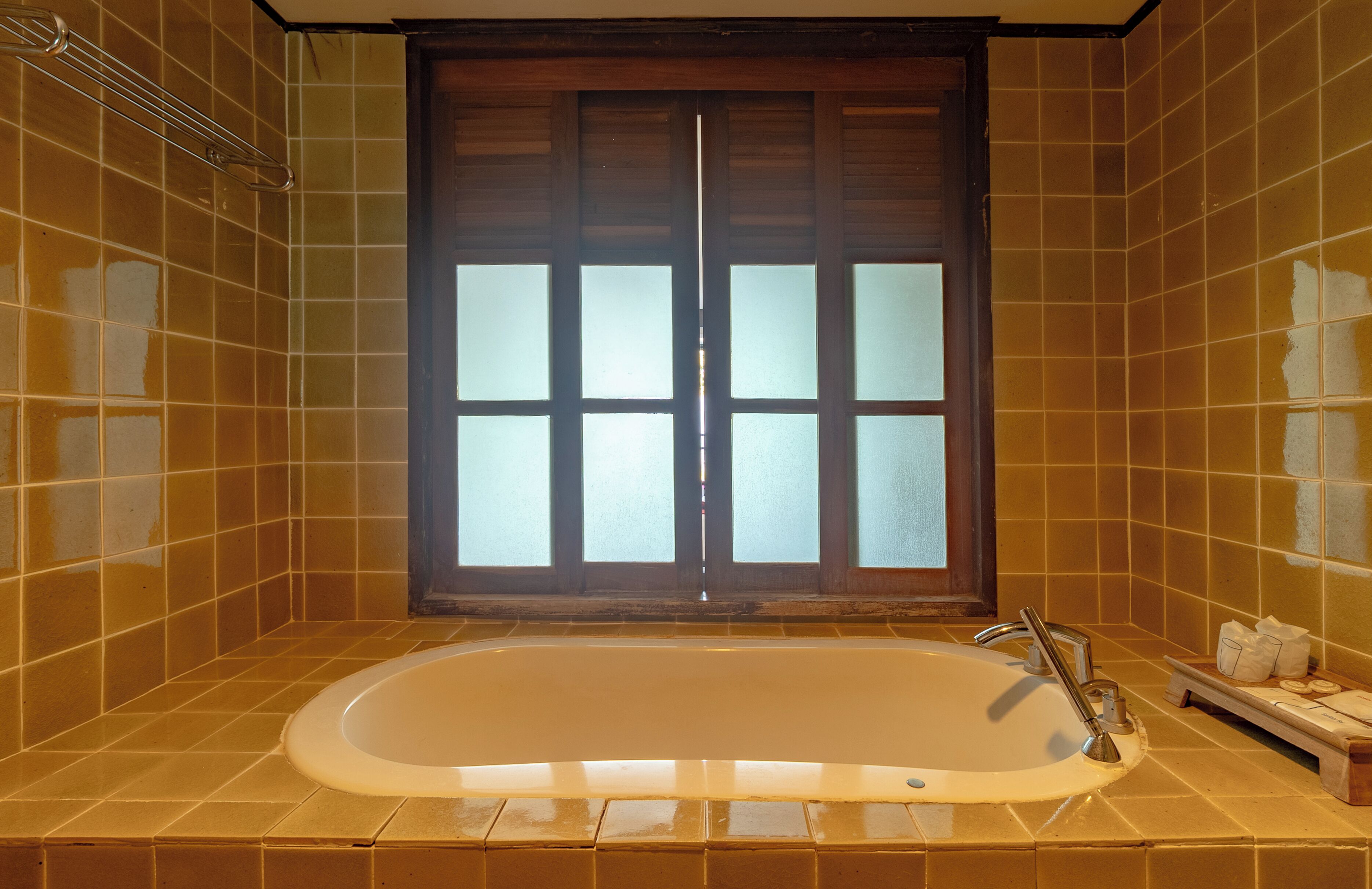 A bathroom with a bathtub, a window with frosted glass, and tiled walls.