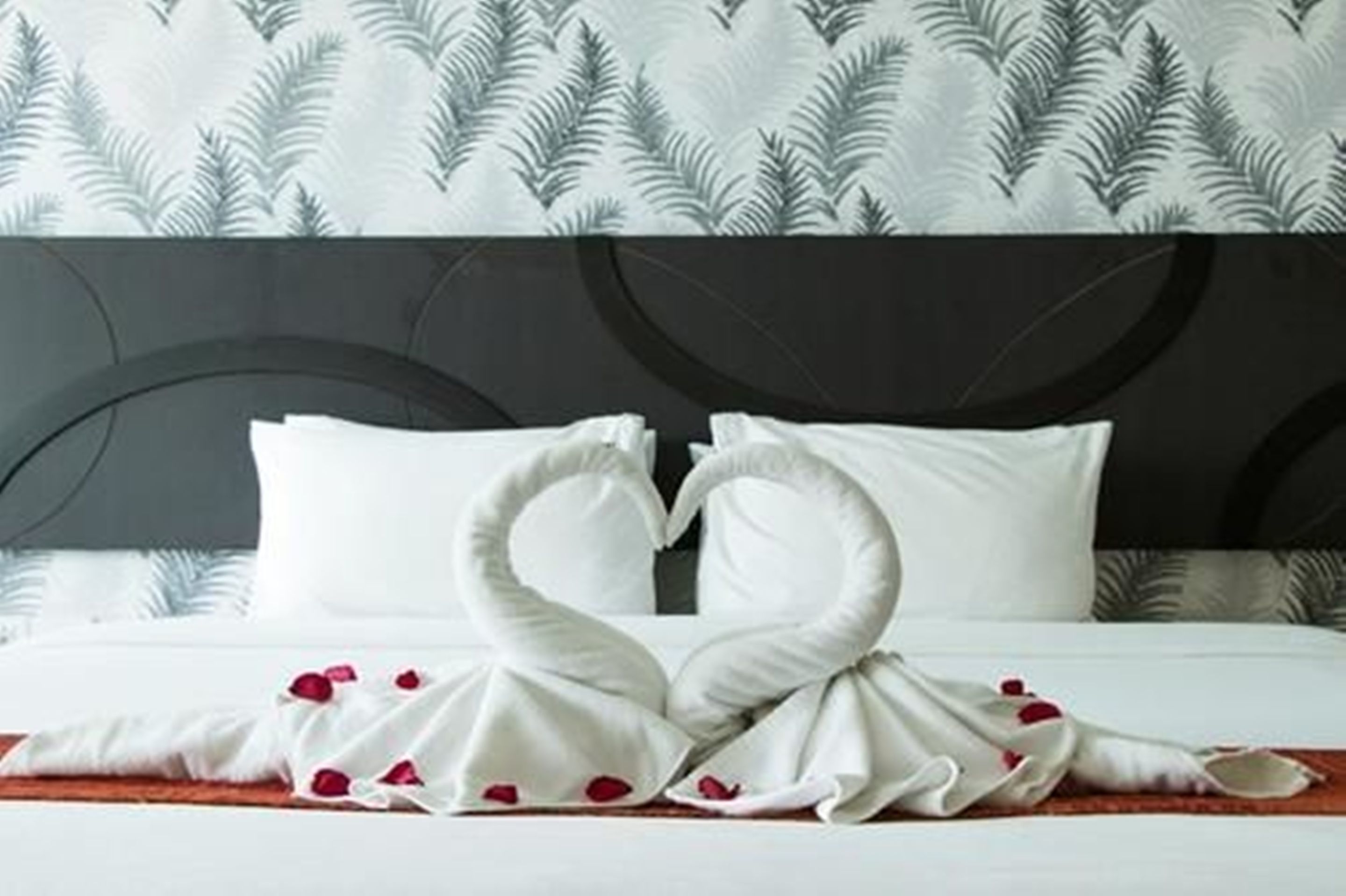 Una habitación de hotel con cama, almohadas blancas y cabecera con diseño de hojas.