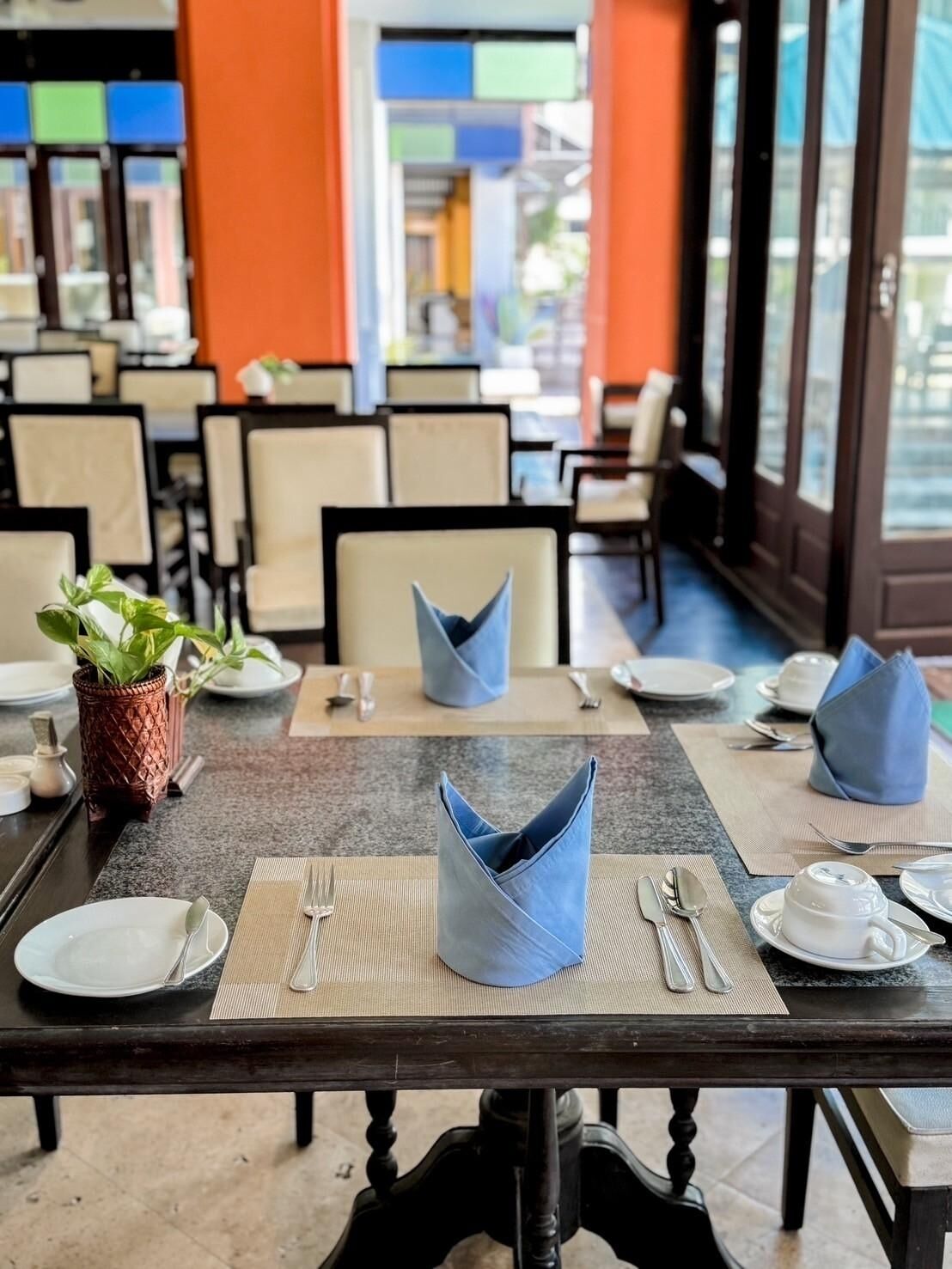 A dining area with tables set for two, featuring a modern design with blue napkins and a potted plant on the table.