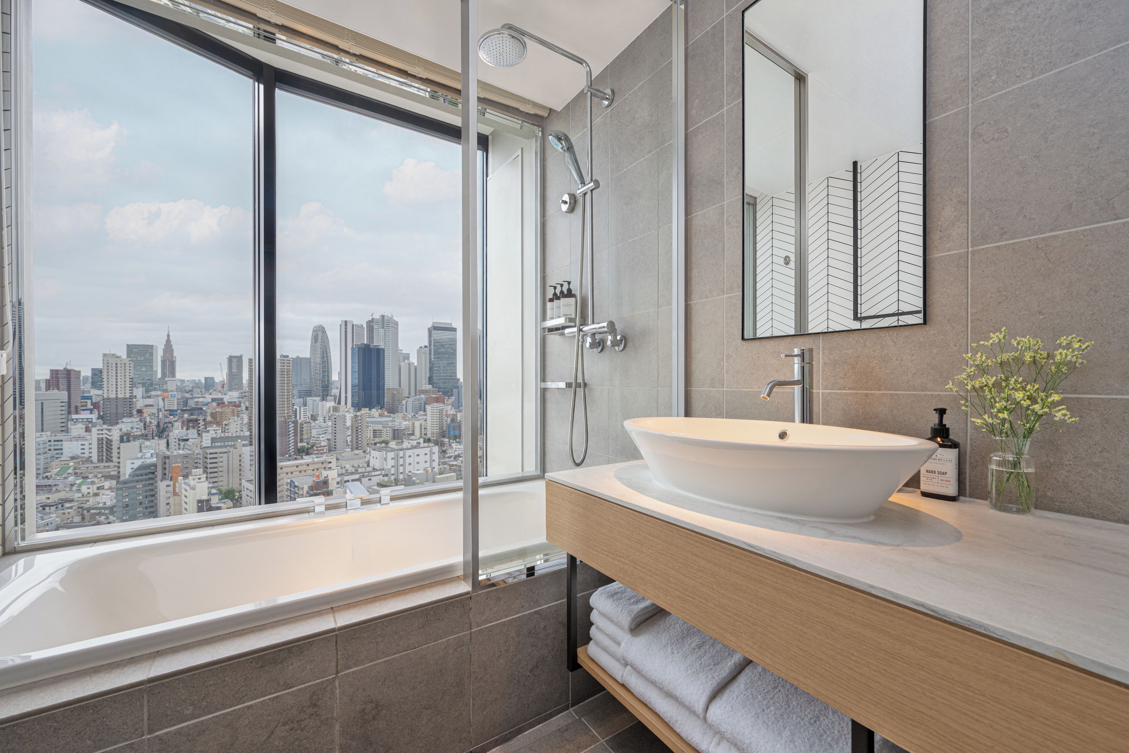 A modern bathroom with a large window, a bathtub, a shower, and a vanity with a sink.
