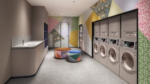 A modern laundry facility with multiple washing machines, a seating area, and a patterned wall design. - Citadines North Shinjuku Tokyo (Tokyo)
