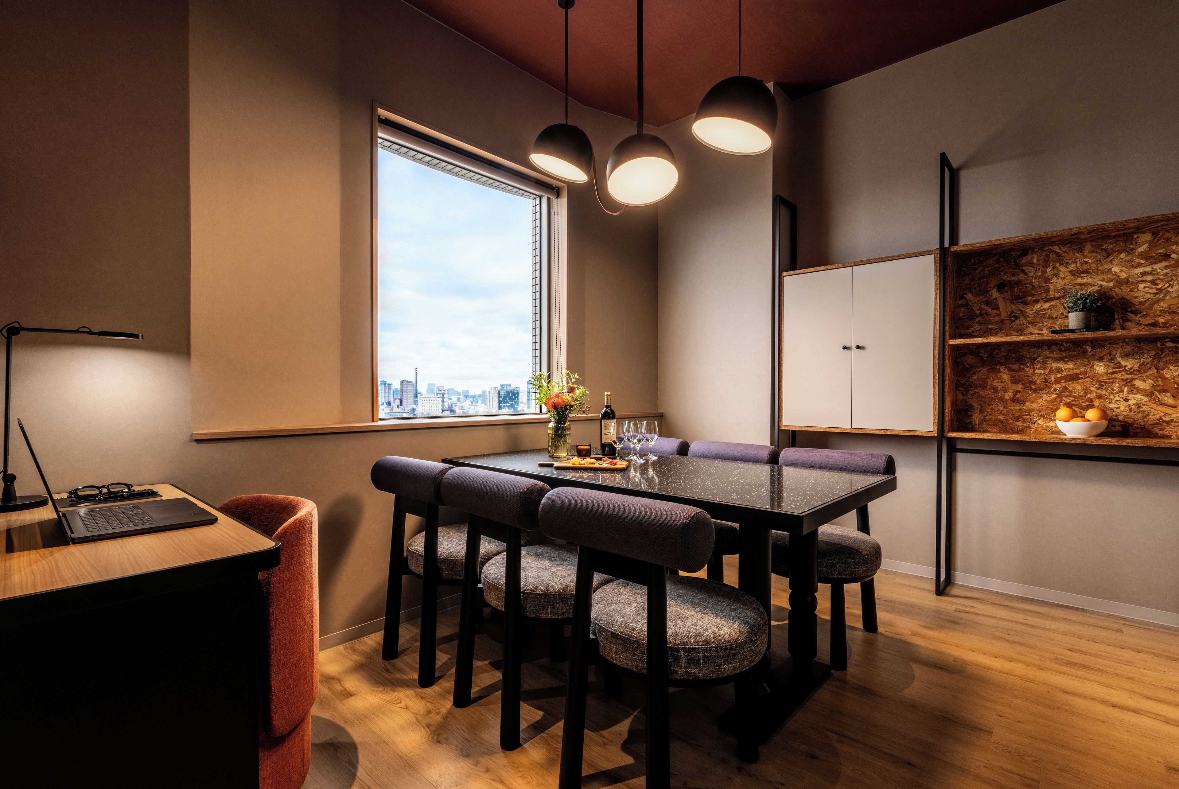 Un comedor moderno con vistas a la ciudad, una mesa de madera y un ordenador portátil sobre un escritorio.