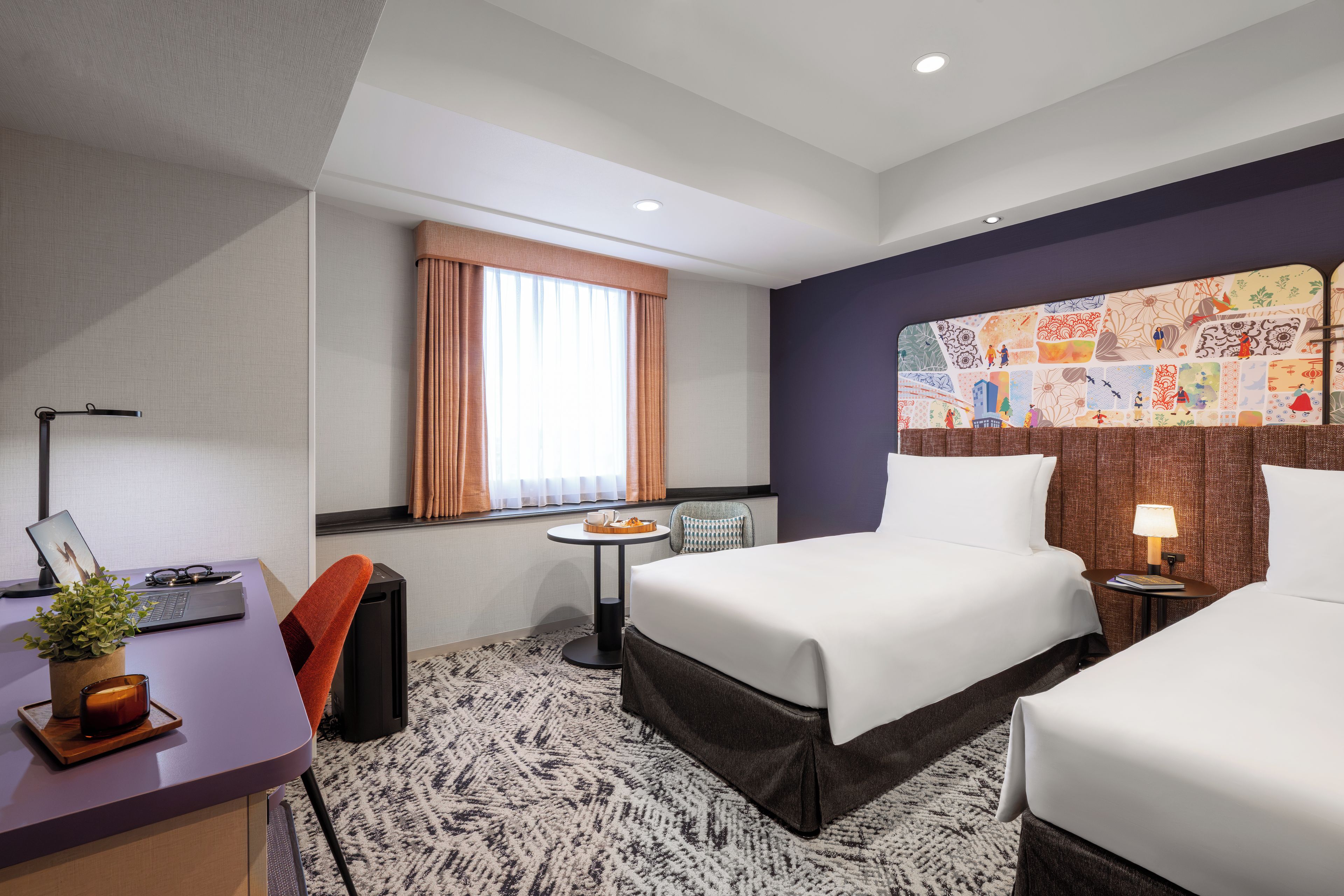 Habitación de hotel con dos camas, un escritorio con una computadora portátil, una mesita con una bandeja, una ventana con cortinas y una decoración en la pared.