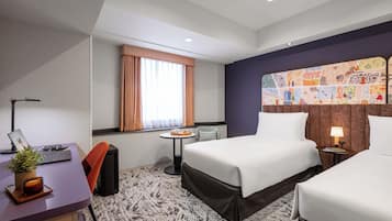 A hotel room with two beds, a desk with a laptop, a small table with a tray, a window with curtains, and a decorative wall.