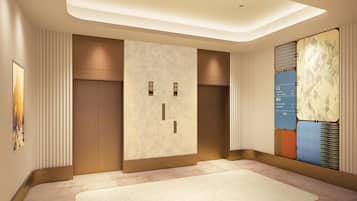 A hotel lobby with a reception desk, a wall-mounted information board, and a large abstract artwork.