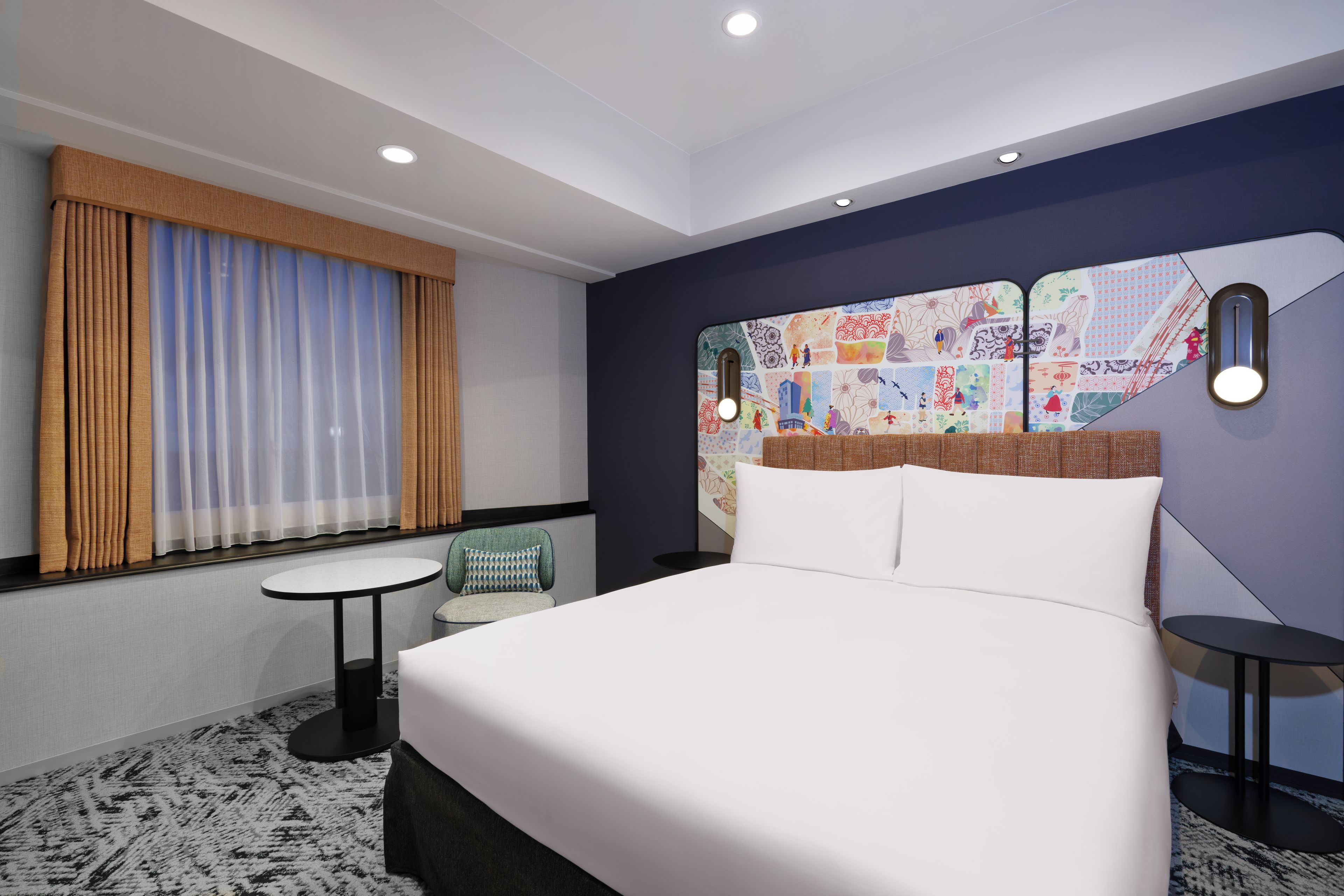 A hotel room with a large bed, a small table, a chair, and a decorative wall.