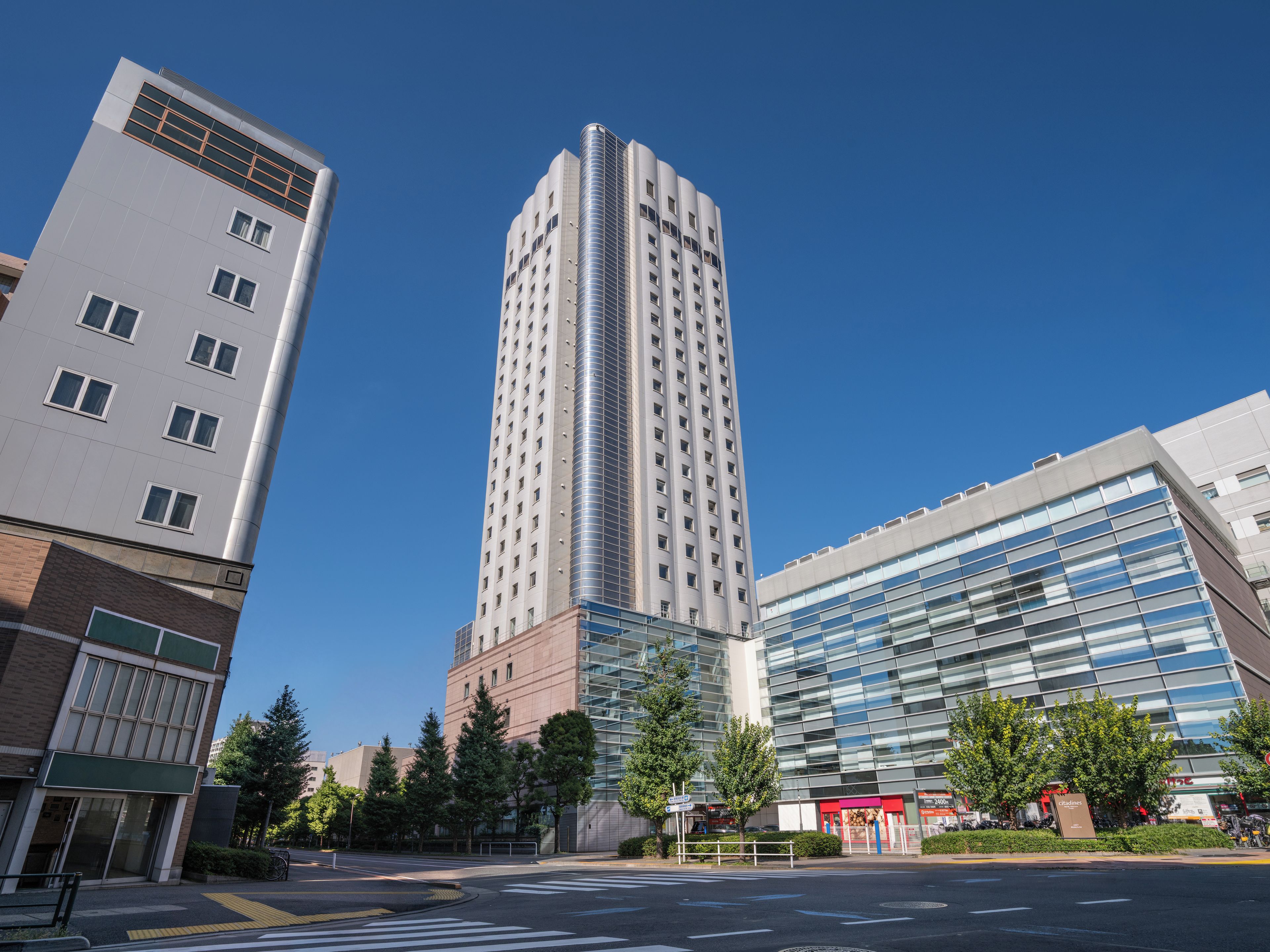 A modern high-rise building with a glass facade, surrounded by other contemporary buildings and a clear sky.
