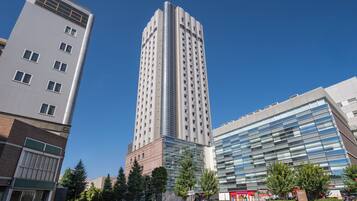 A modern high-rise building with a glass facade, surrounded by other contemporary buildings and a clear sky.