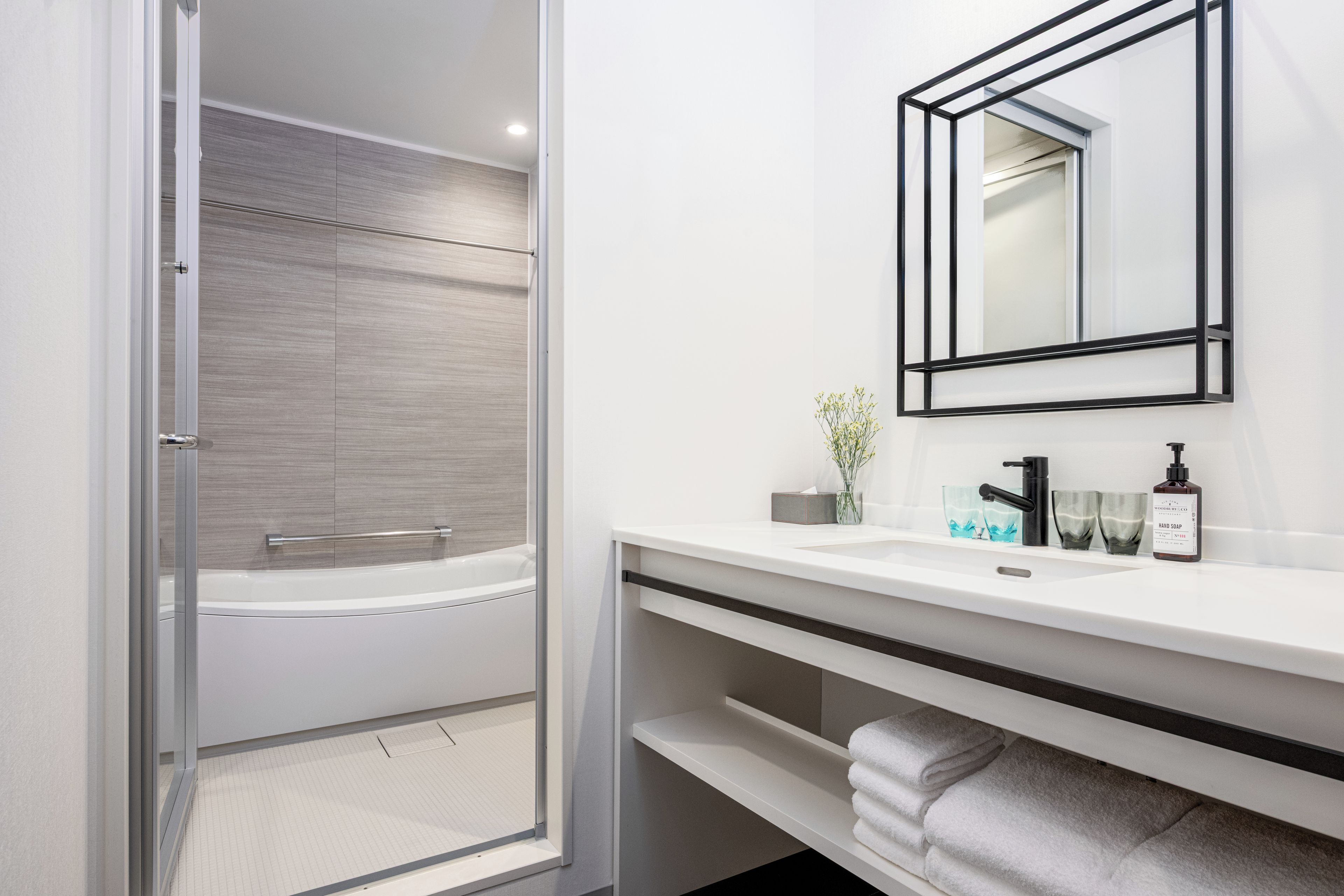 Un baño moderno con cabina de ducha de vidrio, tocador blanco con grifo negro y espejo con marco negro.