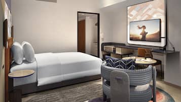 A modern hotel room with a bed, a desk, a television, and a seating area.