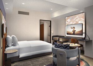 A modern hotel room with a bed, a desk, a television, and a seating area.