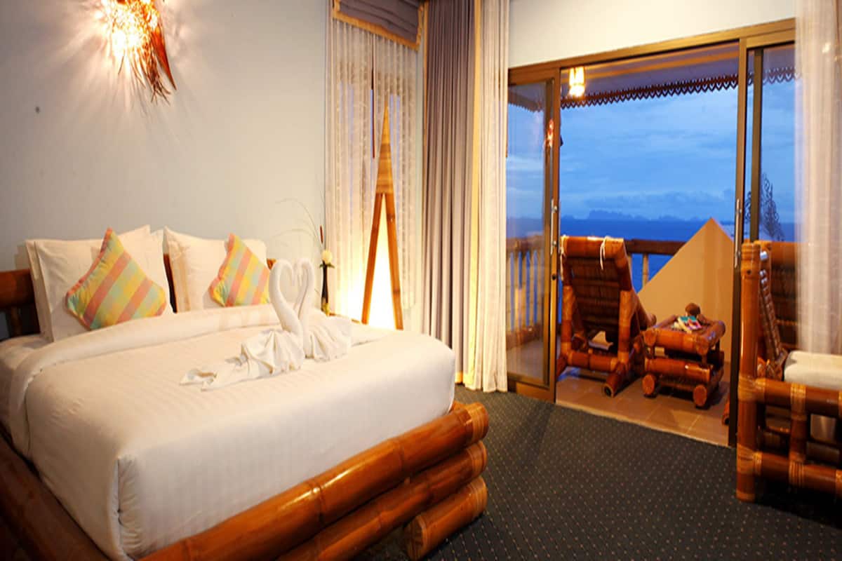 A hotel room with a large bed, a wooden headboard, and a balcony with wicker furniture.