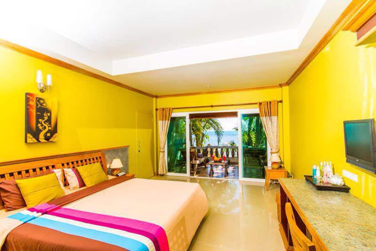 A hotel room with a bed, a TV, a desk, and a balcony with a view of the ocean.