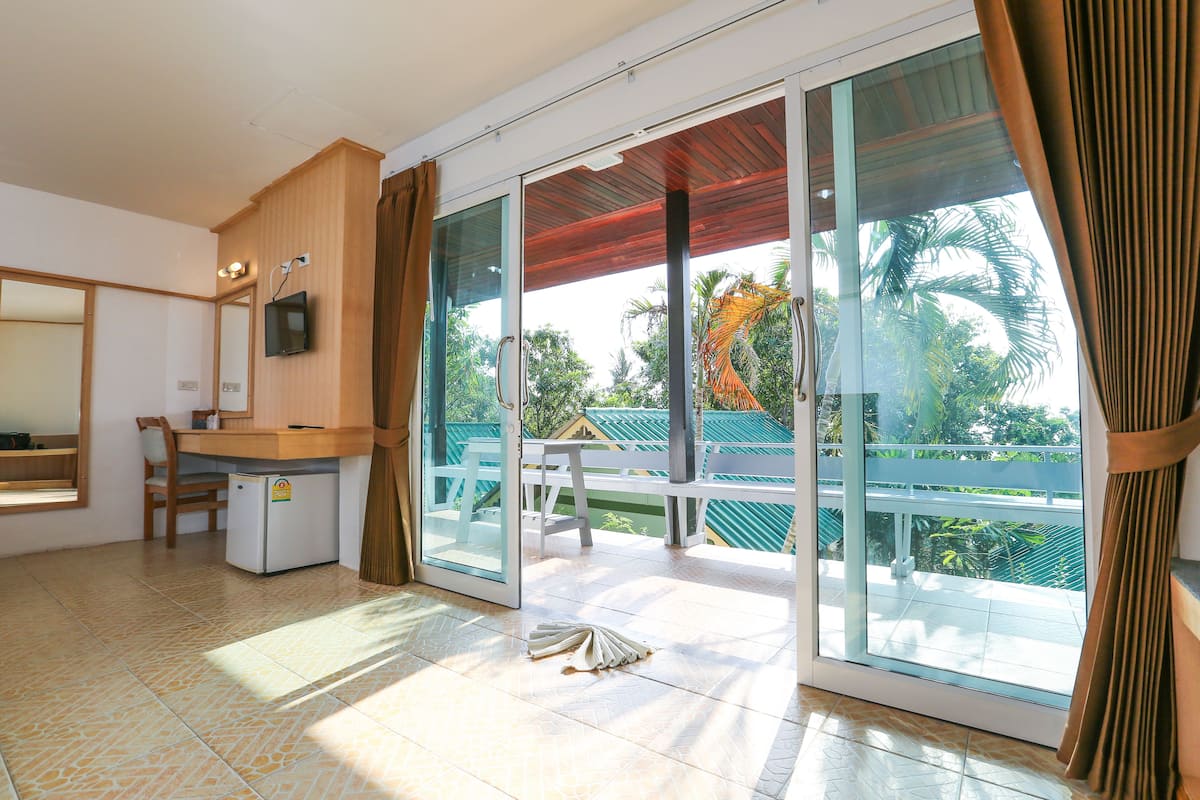 A room with a sliding glass door leading to a balcony, a small refrigerator, a wooden desk, and a chair.