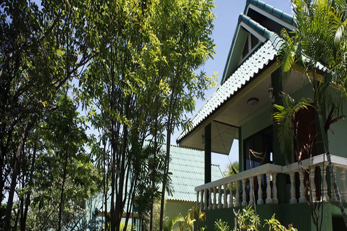 A house with a green exterior, a white balcony, and a tiled roof.