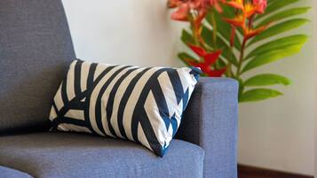 A grey sofa with a striped pillow and a plant with red flowers in the background.