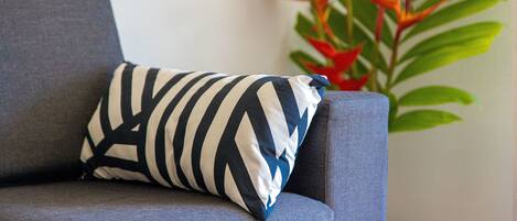 A grey sofa with a striped pillow and a plant with red flowers in the background.