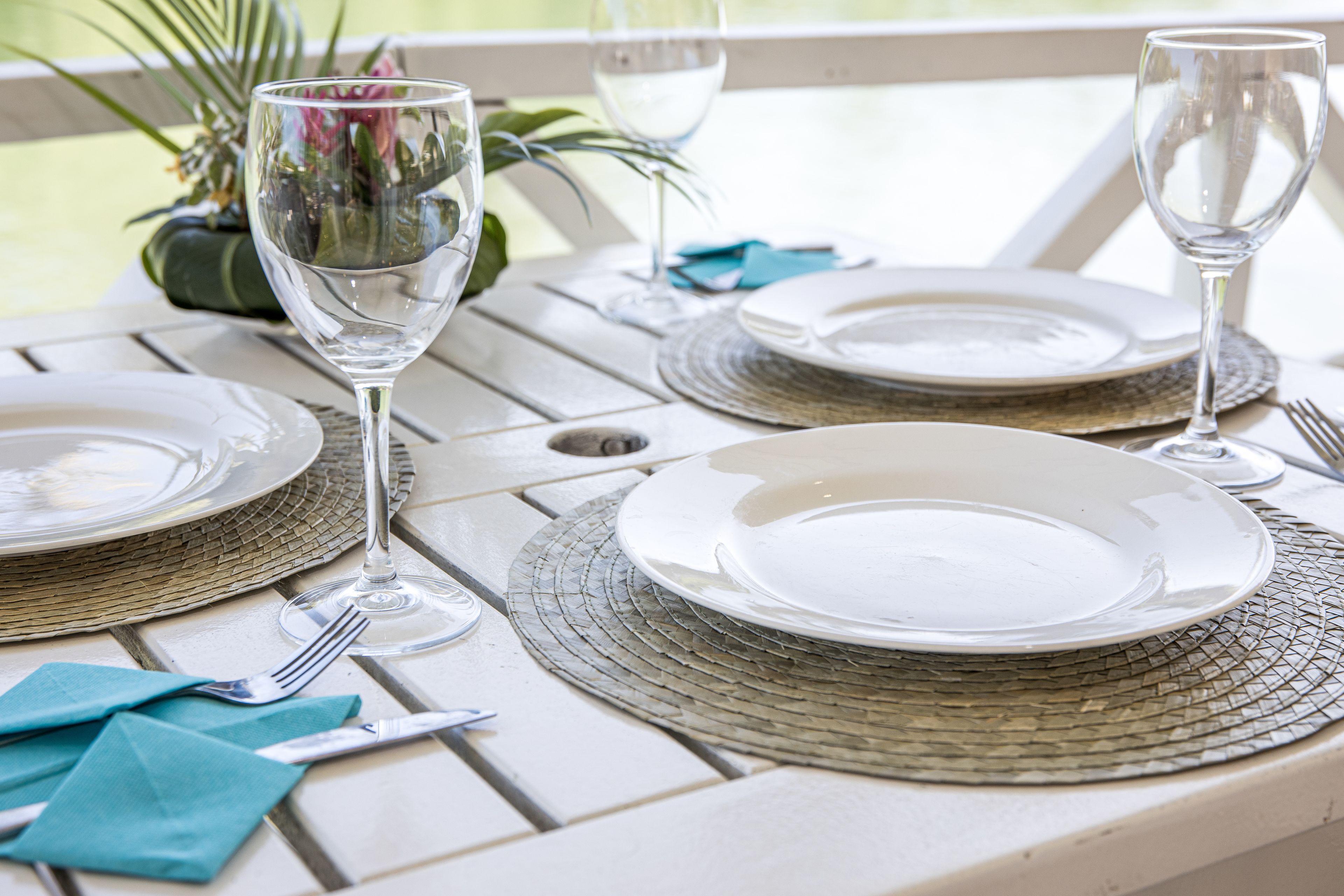 A dining table set with plates, cutlery, and wine glasses, with a woven placemat underneath.